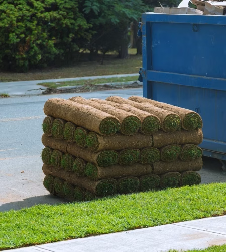 Installation of a modern landscape stacks of sod rolls for new lawn and dumpster full garbage container residential building construction home
