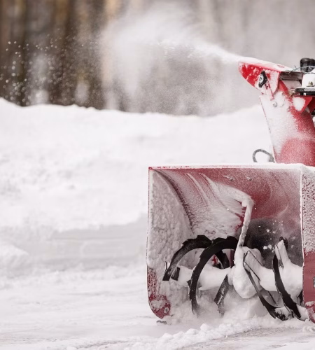 A man with a red snow-covered snow blower clears the area from snow. Clearing the area from snowfall.